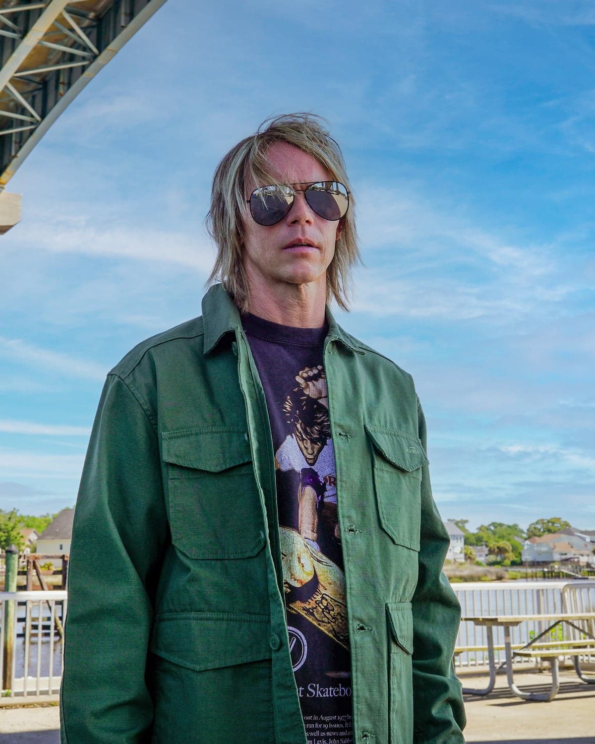 Brad Cox, in sunglasses and a green field jacket, beneath a road bridge